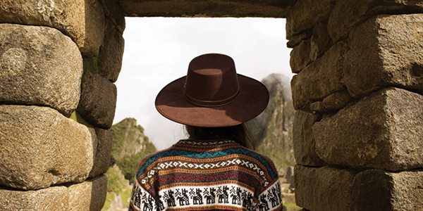 A woman in a hat walking through a stone archway