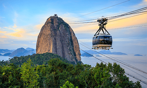A cable car soars through the air, above the lush trees to get to Sugarloaf Mountain