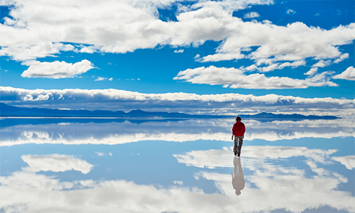 A person walks on the Bolovia Salt Flats, as the sky is beautifully reflected off of the flat's floor