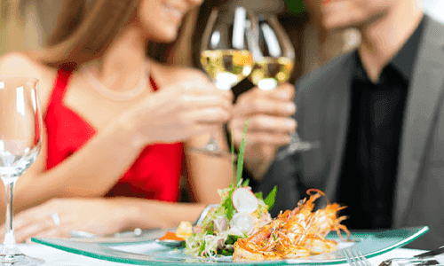 A couple cheers their wine glasses while they sit down at an exquisite meal