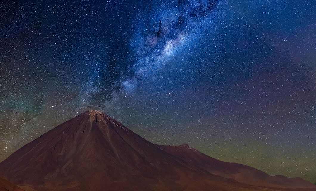 A mountain peak stands under a clear night sky near La Paz, with the Milky Way galaxy stretching brightly overhead and countless stars, offering a mesmerizing view reminiscent of an Atacama Desert tour.
