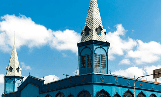 A blue building with two pointed silver spires and arched windows stands against a bright sky with scattered clouds—an ornate landmark you might see on a Guianas Tour.