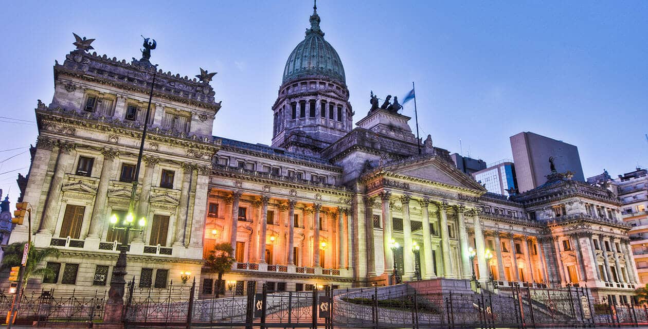 The illuminated exterior of the Argentine National Congress building in Buenos Aires at dusk, featuring a large central dome, neoclassical columns, and the Argentine flag—a stunning sight for any honeymoon journey.