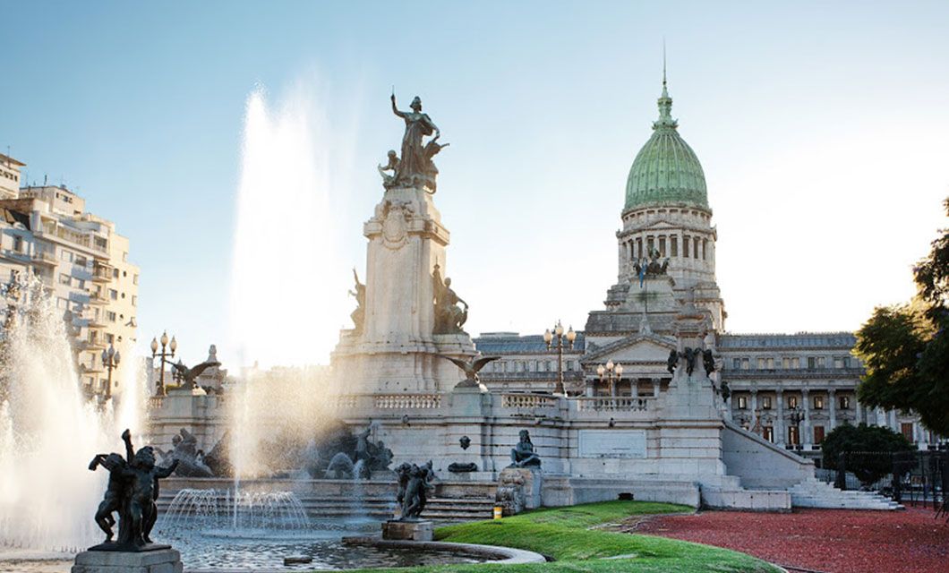 The image shows the National Congress building in Buenos Aires, Argentina, with its green dome, a large monument and fountain in the foreground—an iconic sight for travelers heading to Ushuaia or embarking on a Patagonia Cruise under a clear sky.
