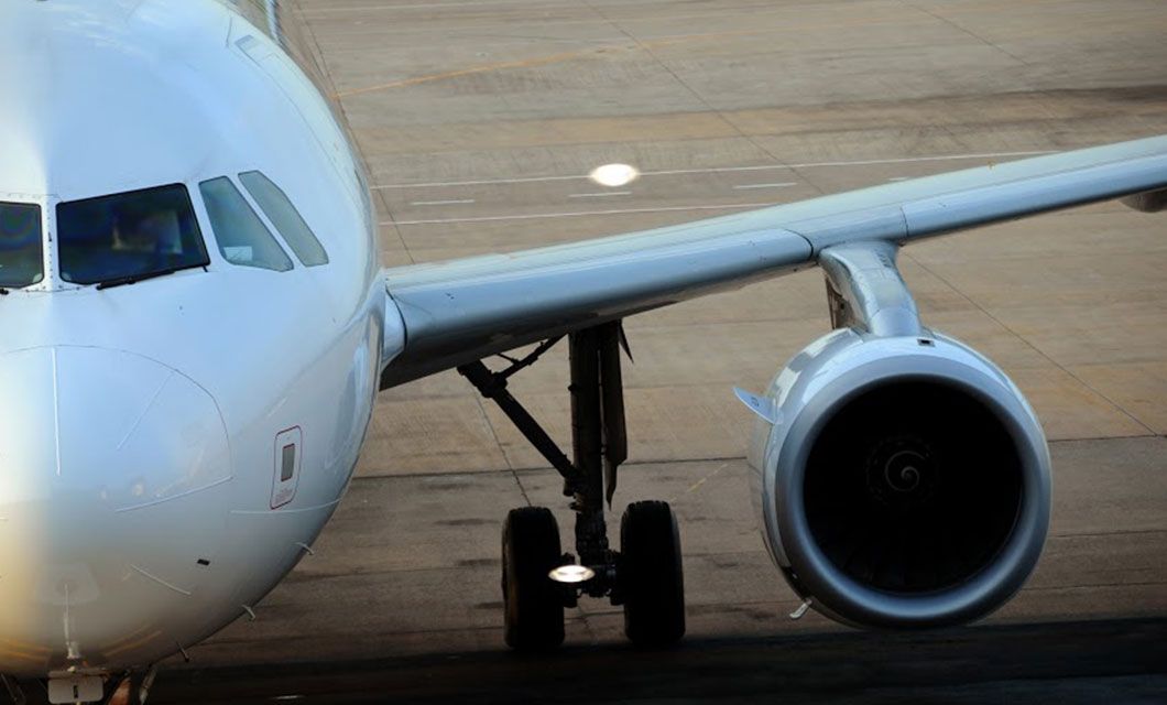 Close-up of a white airplane on the tarmac, showing cockpit windows, front landing gear, and one engine—ready for a Patagonia Cruise adventure or flights to Ushuaia, with the airport runway in the background.
