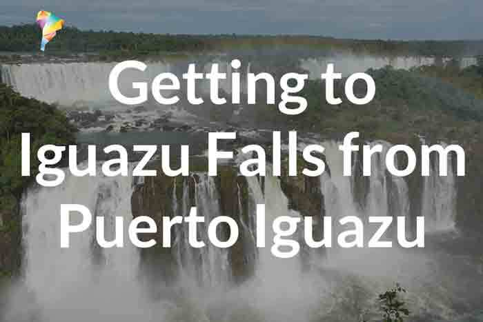 Text over a view of Iguazu Falls reads: Getting to Iguazu Falls from Puerto Iguazu or Buenos Aires. The waterfalls cascade over lush green cliffs under a cloudy sky.