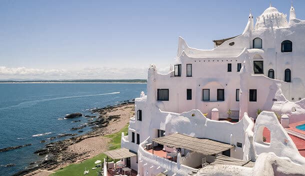White, sculptural building with organic shapes overlooks a rocky coastline and blue ocean under a clear sky. This whimsical, Gaudí-inspired architecture is a highlight of Uruguay—perfect for those on a Brazil Tour or coming from Buenos Aires.