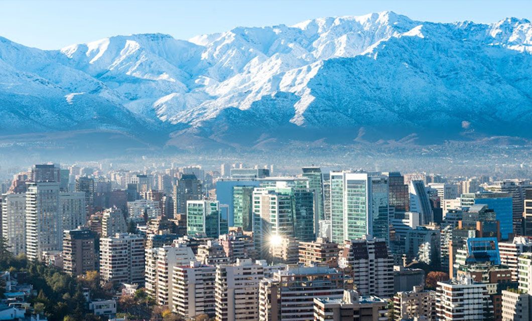 Modern city skyline with tall buildings in the foreground and snow-capped mountains in the background under a clear blue sky, capturing the spirit of Ushuaia and its gateway to Patagonia Cruise adventures.