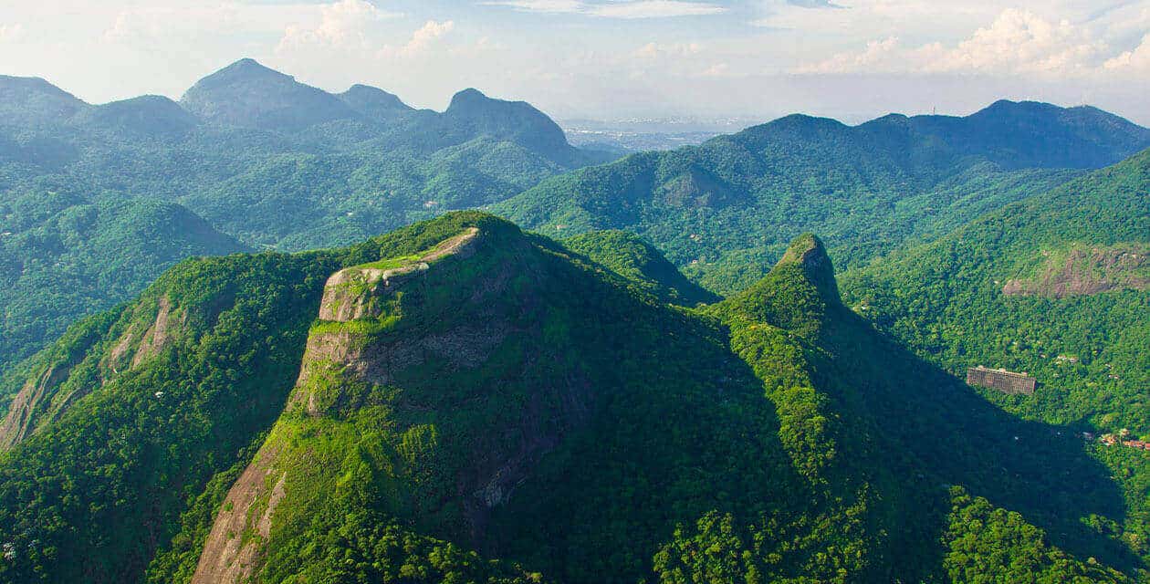 Aerial view of lush green mountains under a partly cloudy sky, with a distinct ridge and dense forest covering the slopes—an inviting landscape for those exploring Uruguay or on a scenic Brazil Tour.