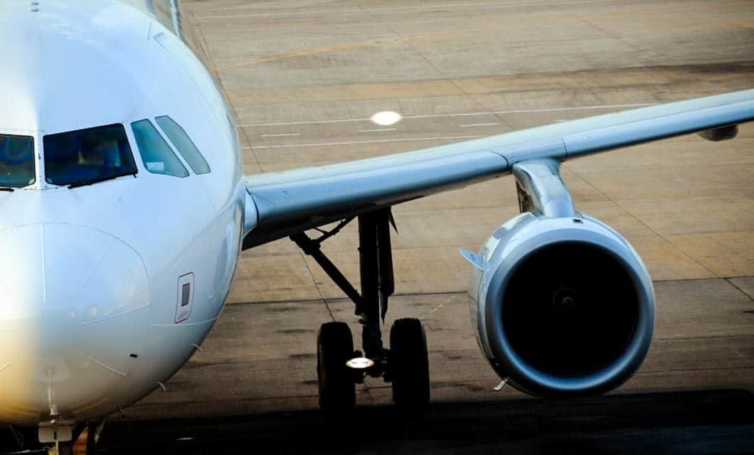 Close-up view of the front section of a white airplane on an airport tarmac in Argentina, the Land of Contrast, showing its cockpit windows, nose, one engine, and landing gear.