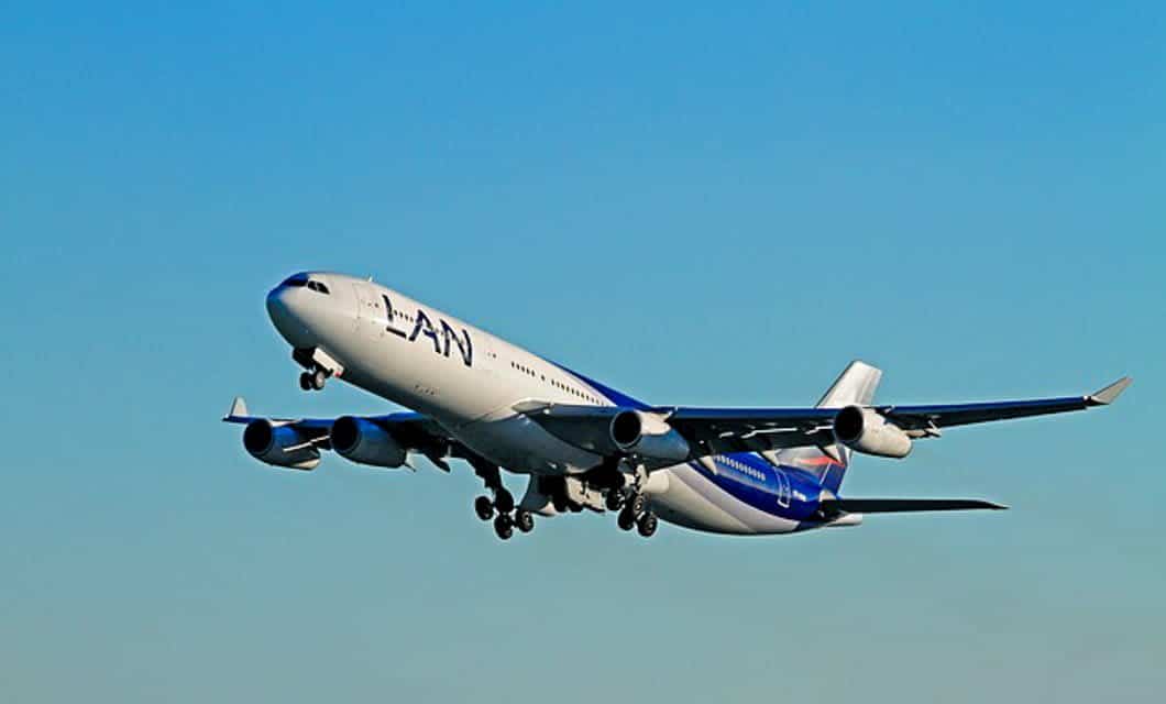 A large commercial airplane with ANA livery is taking off against a clear blue sky over Florianopolis, its landing gear still visible.