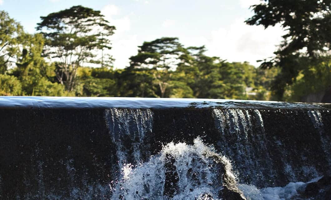 A close-up view of water cascading over a low waterfall in Manu National Park, with trees in the background under a partly cloudy sky in the Peruvian Amazon.