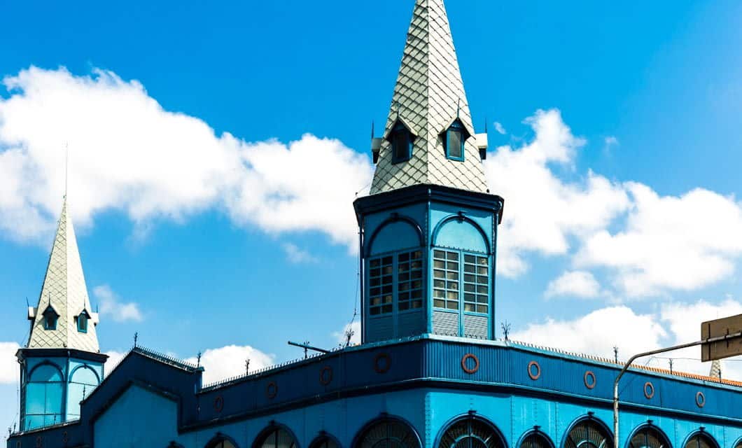 A vibrant blue building with two tall, pointed towers and decorative windows stands against a bright sky with scattered white clouds in Salvaterra on Marajó Island.