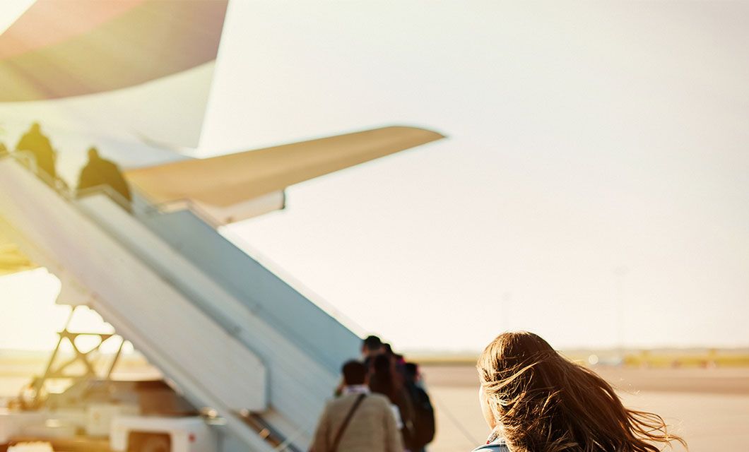 A group of people board an airplane via a mobile staircase on a sunny day in Bariloche; one person with long hair is seen from behind in the foreground, ready to embark on their Patagonia Tour.