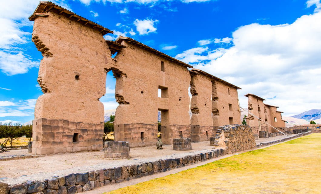 Ancient adobe and stone ruins of the Raqchi archaeological site in Peru, showcasing tall, partially destroyed walls under a bright blue sky—an enduring testament to Peruvian culture.