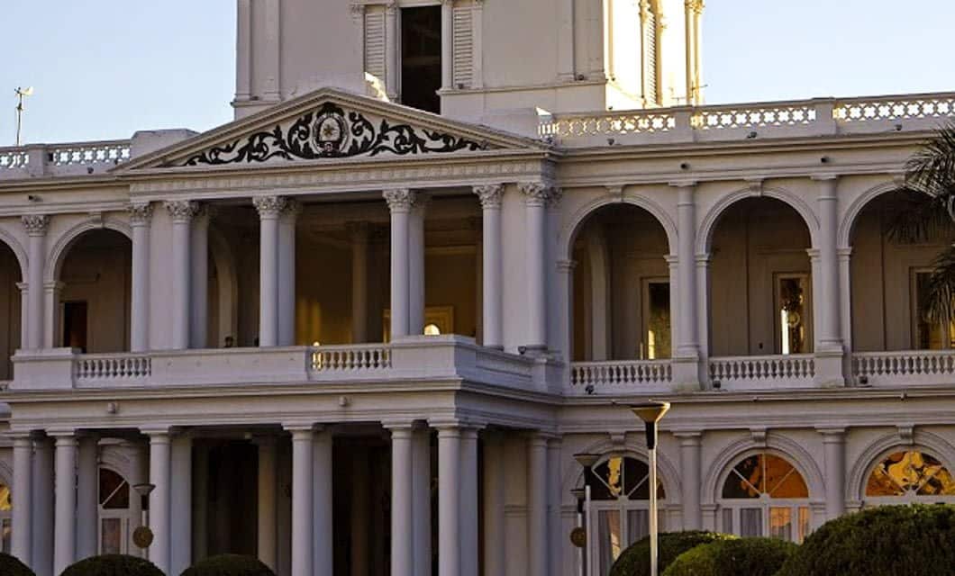 A grand white colonial-style building with tall columns, arched balconies, and ornate railings, reminiscent of Paraguay’s stately architecture and perfect for a tour before heading to the natural wonders like Iguazu Falls.