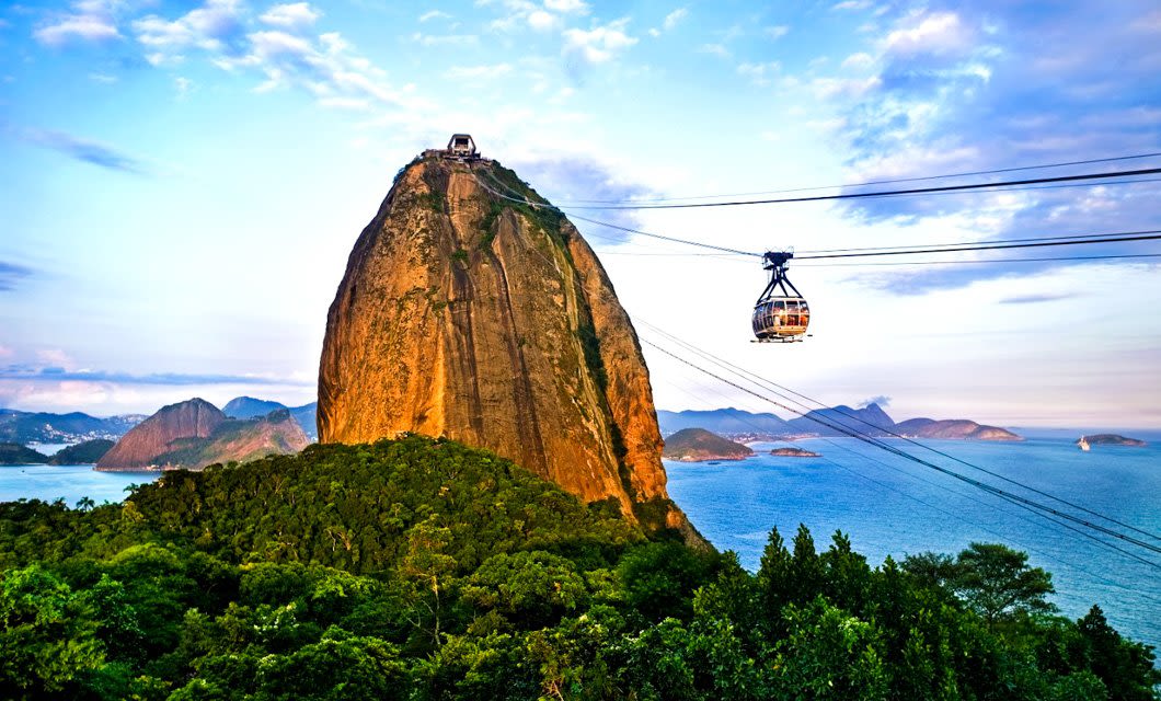 A cable car ascends Sugarloaf Mountain in Rio de Janeiro, Brazil, overlooking lush green forests and blue ocean—a breathtaking view just a short trip from colonial highlights and the famed Brazil coffee region.