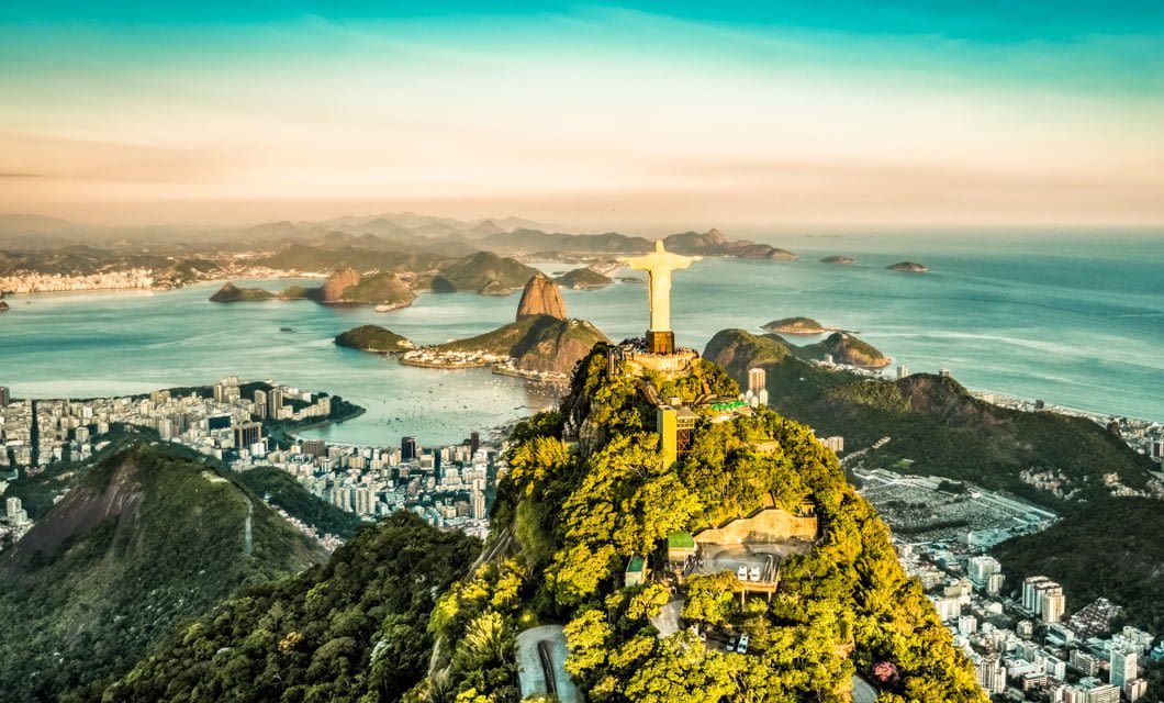 Aerial view of Rio de Janeiro featuring the Christ the Redeemer statue atop Corcovado Mountain, lush green hills, city buildings, and the coastline with blue ocean—Brazil’s beauty stretching from Pantanal wetlands to distant mountains.