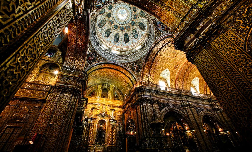 Ornate interior of a historic building with intricate golden carvings, arched columns, and a large, decorated dome ceiling illuminated by natural light from above—reminiscent of landmarks visited on a Machu Picchu adventure.