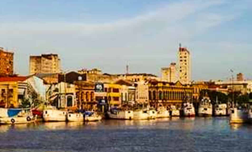 A waterfront cityscape in Belém with boats docked along the shore, historic and modern buildings in the background, all under a blue sky with soft clouds—gateway to Marajó Island and nearby Salvaterra.