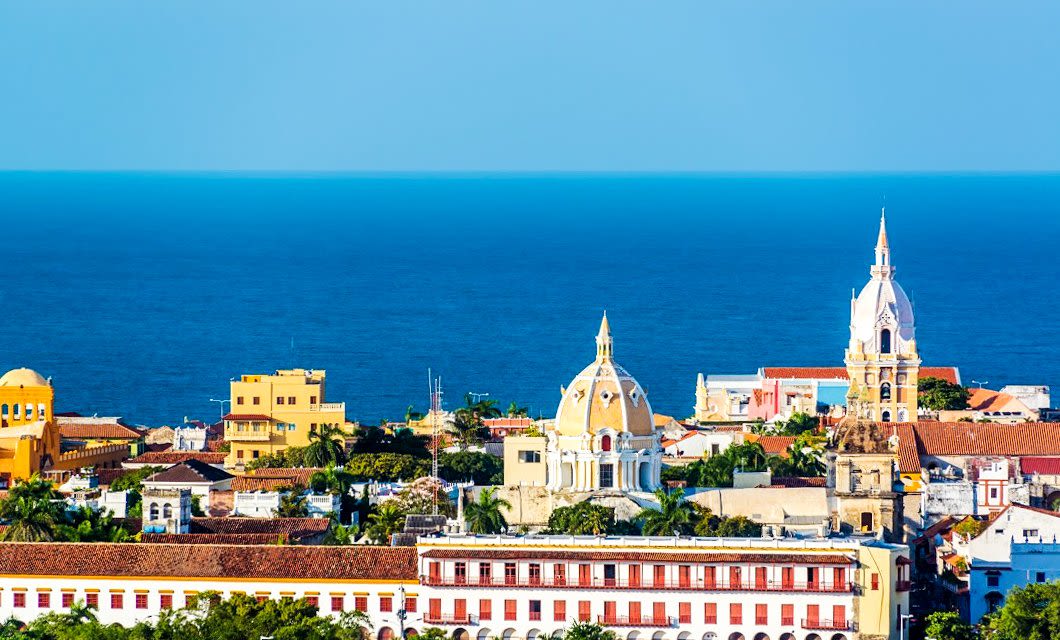 Colorful colonial buildings and historic churches with domes and spires stand against a backdrop of deep blue ocean and clear sky in Cartagena, Colombia—a perfect stop on any Caribbean tour.