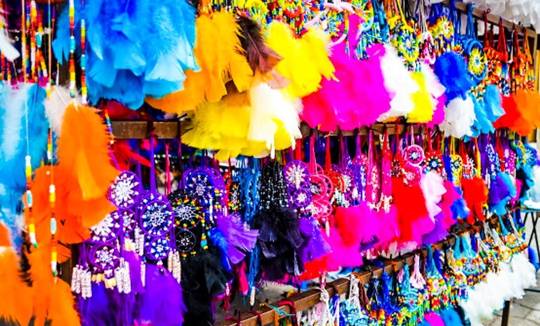 Colorful feathered dreamcatchers and beaded decorations hang closely together at a market stall in Quito, brightening any Ecuador Tour with vibrant shades of yellow, blue, pink, orange, and purple.