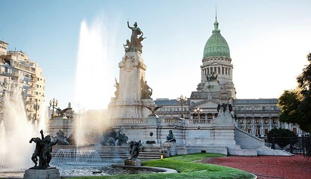 The image shows the Argentine National Congress building with its green dome, a large fountain, and statues in the foreground, under a clear sky in Buenos Aires—the perfect starting point for a family journey to the end of the world.