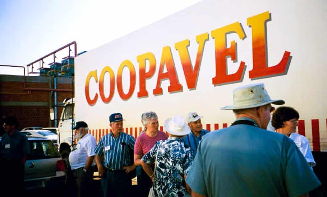 A group of people, mostly older adults in casual clothes and hats, stand next to a large white truck with COOPAVEL written in bold red and yellow letters—part of a Brazil Agriculture Tour at the Coopavel Show Rural.