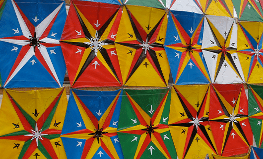 A close-up view of a colorful display of geometric kites arranged in rows, each with star and arrow patterns in various bright colors like blue, red, yellow, green, and white.