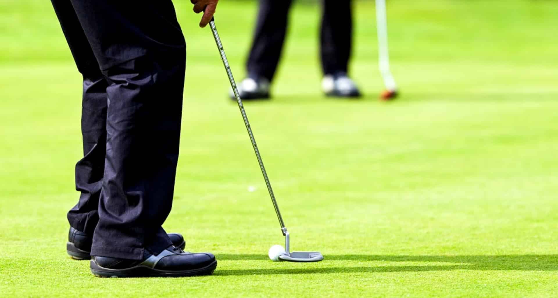A close-up of a golfer preparing to putt on a green during one of the Chile Golf Tours, with another golfer standing in the background. Both are wearing dark pants and golf shoes.