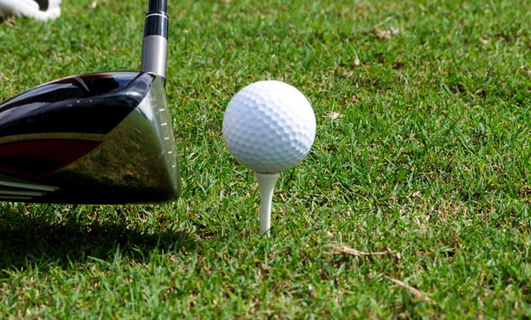 A close-up of a golf driver positioned next to a golf ball on a tee, set on green grass, ready for a shot during the Brazil Golf Tour.