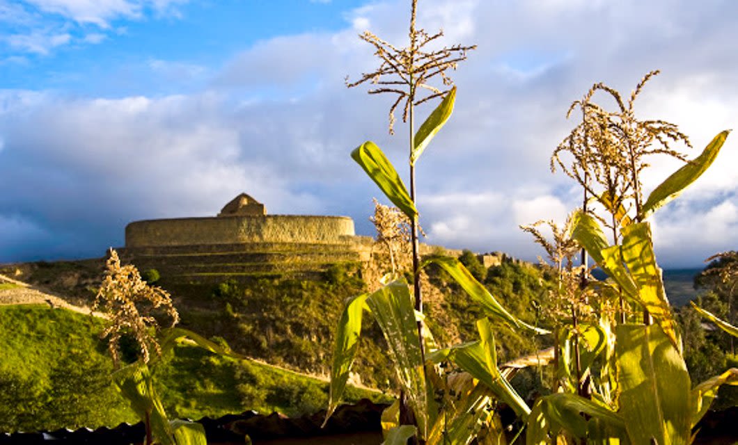 Ancient stone fortress on a hill under a cloudy sky, with green corn plants in the foreground, reminiscent of Frederic Edwin Church’s Andes painting Heart of the Andes.