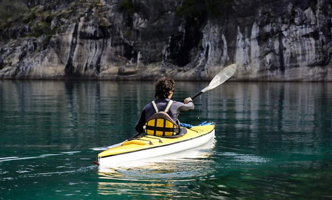 A person with curly hair paddles a yellow kayak on calm, clear water near rocky cliffs in Santa Catarina, surrounded by nature—perfect for a Brazil Adventure Tour.
