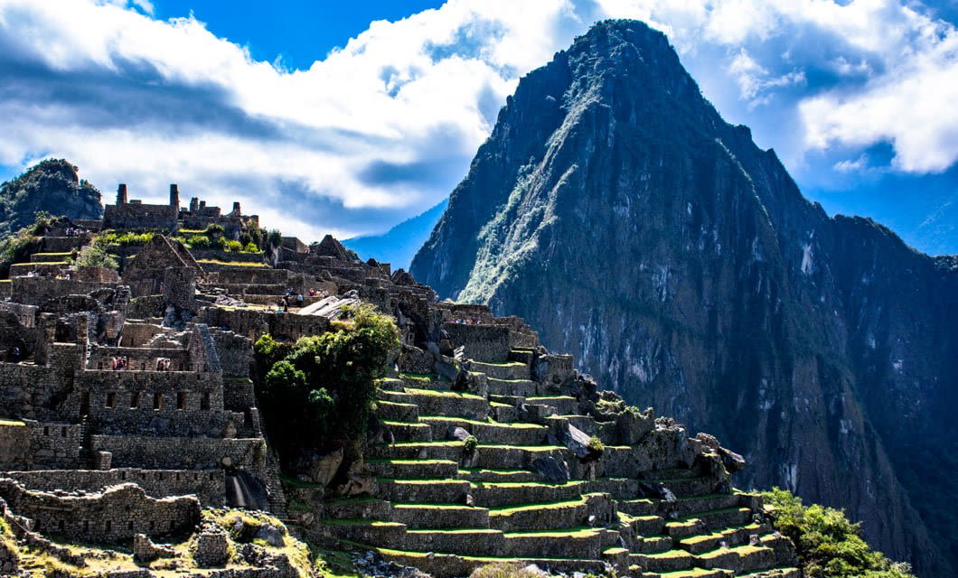 Ancient stone ruins of Machu Picchu sit on green terraced slopes, with a tall, steep mountain rising dramatically in the background—an unforgettable sight on your tour before venturing into the nearby Amazon Jungle.