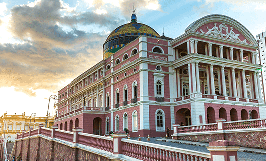 A grand pink and white neoclassical building with columns and a domed roof rises under a partly cloudy sky—the Amazon Theatre in Manaus, Brazil, a stunning landmark often visited during an Amazon Rainforest tour.