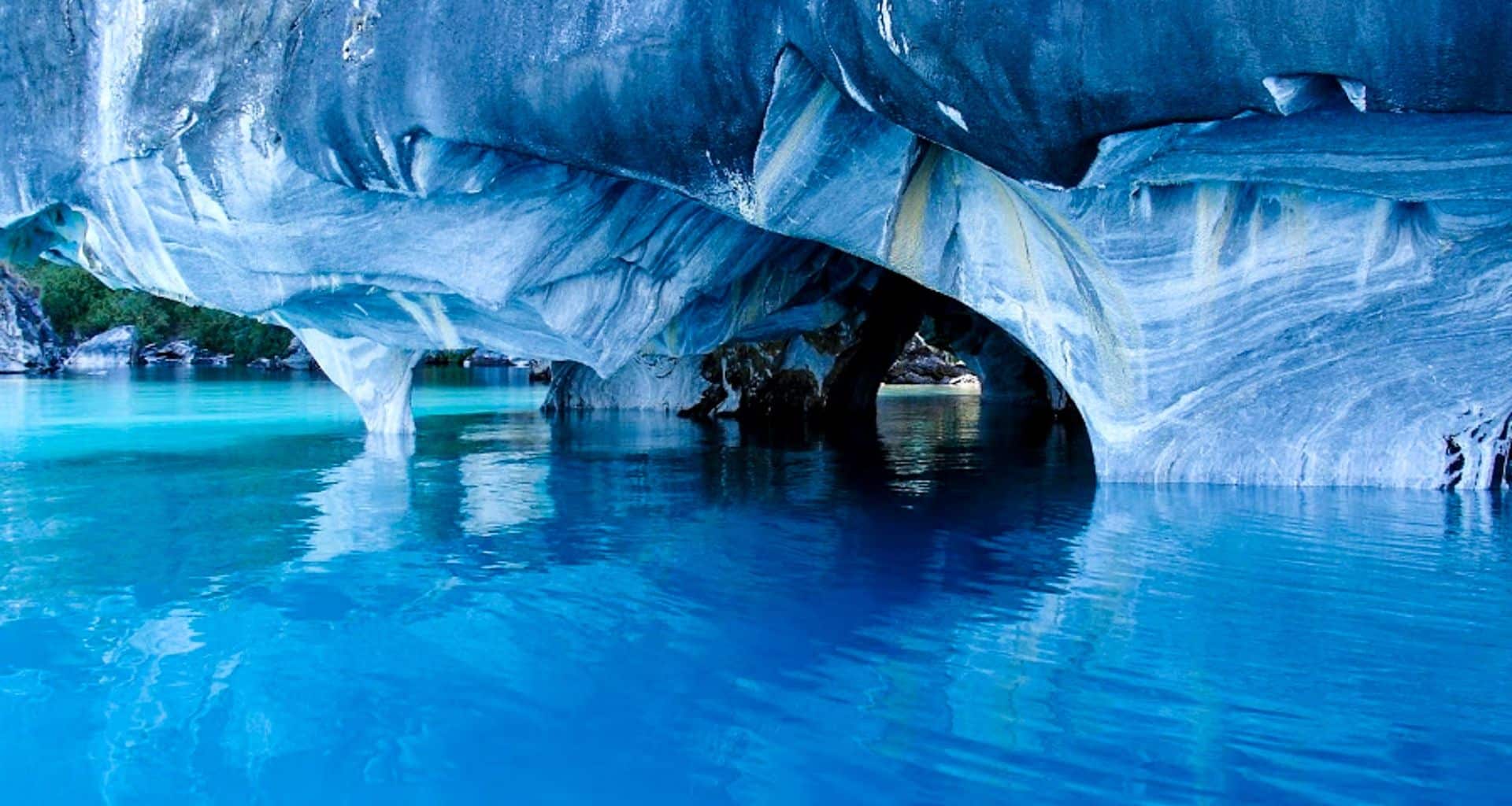 Marble caves with intricate blue and white patterns reflect on vibrant turquoise water below, creating a striking natural scene along the famous Patagonian Route 40—an unforgettable highlight of any Patagonian tour.