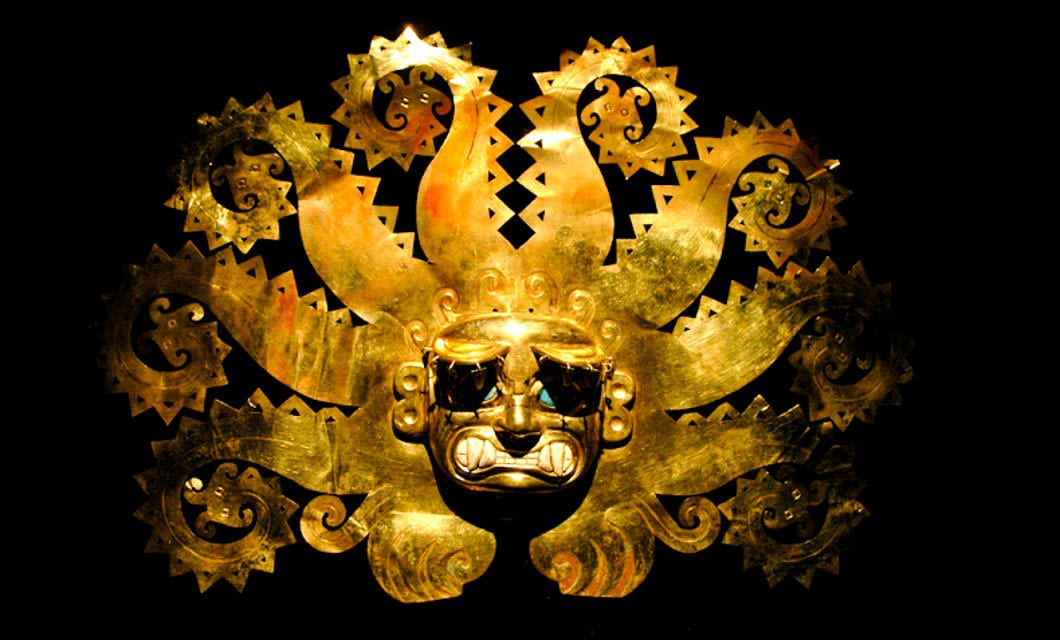 A golden mask with a fierce face and elaborate sunburst design, featuring intricate, jagged rays radiating outward, displayed against a dark background—an artifact echoing the artistry of Cajamarca archaeology.