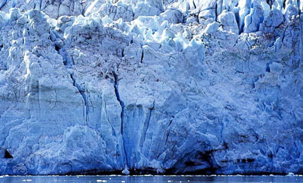 A close-up view of a massive blue glacier with jagged ice formations and cracks, rising above dark cold water dotted with floating ice—a striking scene often witnessed on a Patagonia cruise from Santiago to Buenos Aires.