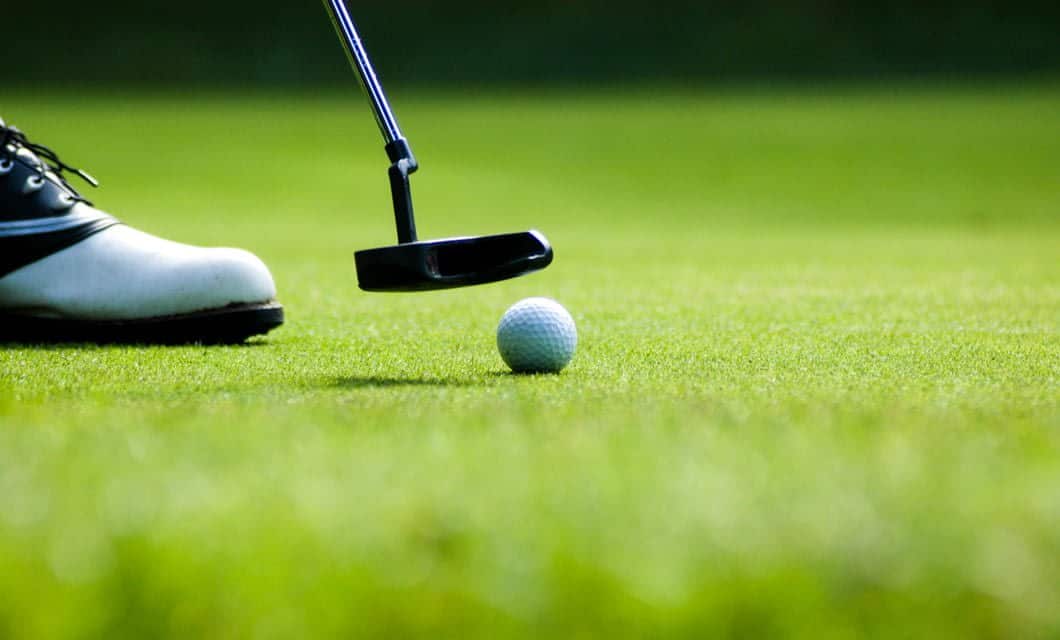 A close-up of a golfer's shoe and putter next to a golf ball on a green, ready to make a putt during a South America Golf Tour.