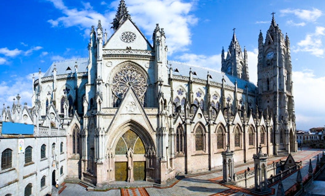 A large Gothic-style cathedral with pointed arches, ornate stonework, and tall spires rises under a blue sky—an architectural marvel to admire before embarking on an unforgettable Luxury Galapagos Cruise from Ecuador.
