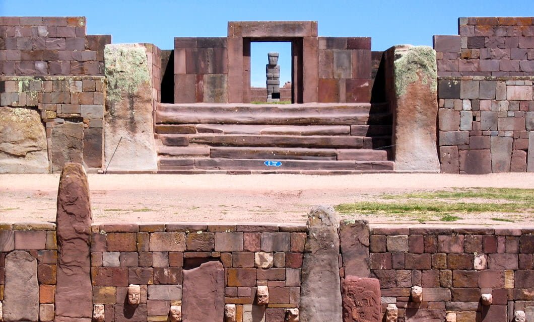 Explore the ancient stone structure at Tiwanaku, Bolivia, on your next travel adventure—featuring a terraced platform, carved stone faces in the foreground, and a statue visible through a stone doorway.