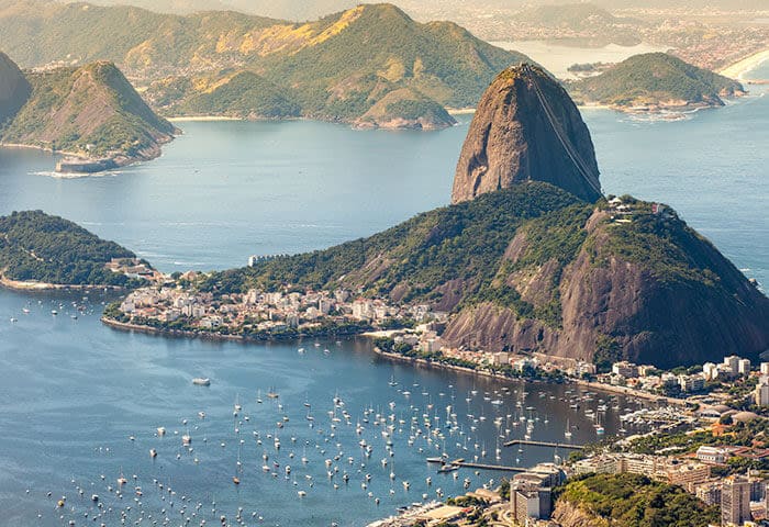 Aerial view of Sugarloaf Mountain rising from the coastline in Rio de Janeiro, one of South America’s cultural capitals, with boats in the bay and green hills in the background.