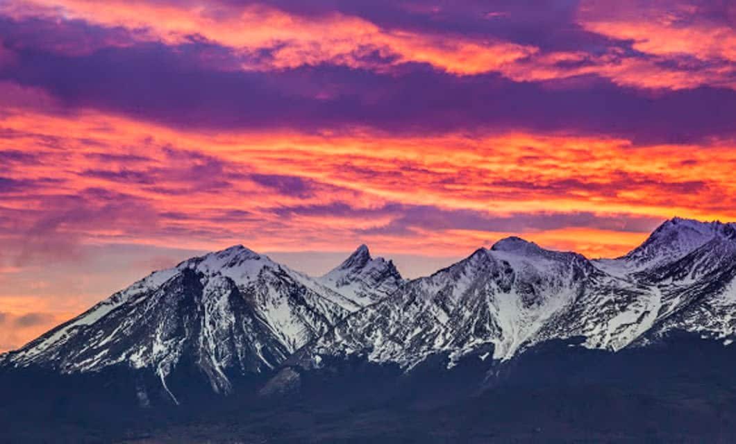 Snow-capped mountains under a dramatic sky at sunset, with vibrant orange, pink, and purple clouds creating a colorful backdrop above the rugged peaks—a view to behold on an Antarctica Cruise departing from Ushuaia.