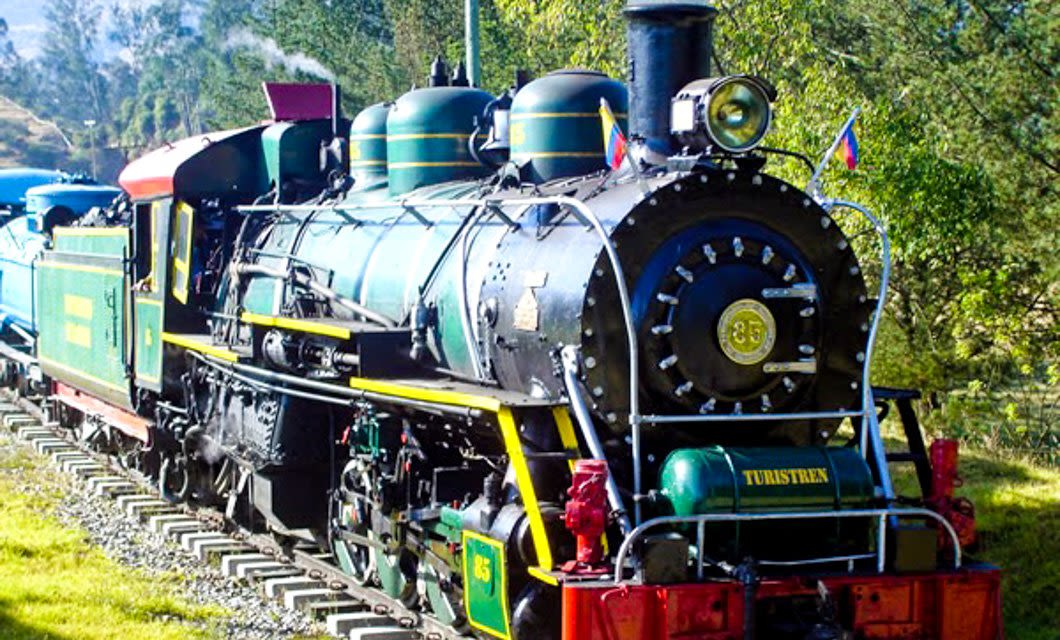 A vintage green and black steam locomotive with yellow accents labeled TURISTREN travels on a railroad track through a lush, green landscape near Bogota, offering a classic Colombia Train Tour under daylight.