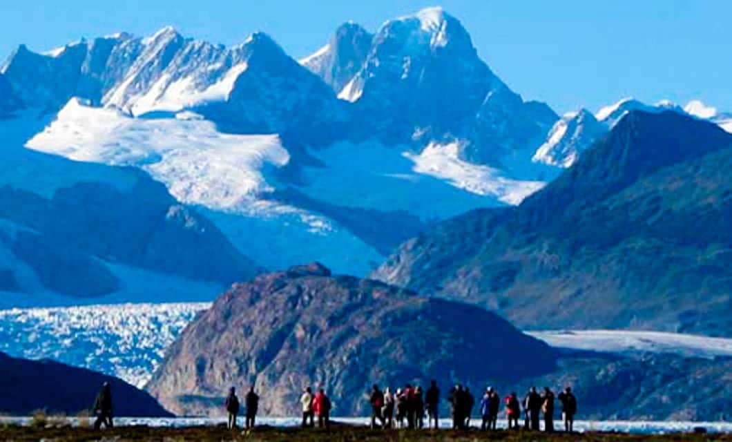 A group of people stands on a rocky plain with snow-capped mountains and glaciers in the background under a clear blue sky, capturing the wild beauty often seen on a Patagonia cruise from Santiago to Buenos Aires.