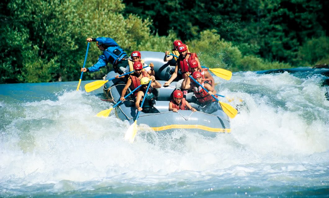 A group of people wearing helmets and life jackets paddle an inflatable raft through whitewater rapids in Salta, Argentina, surrounded by lush trees and greenery on this thrilling adventure tour.