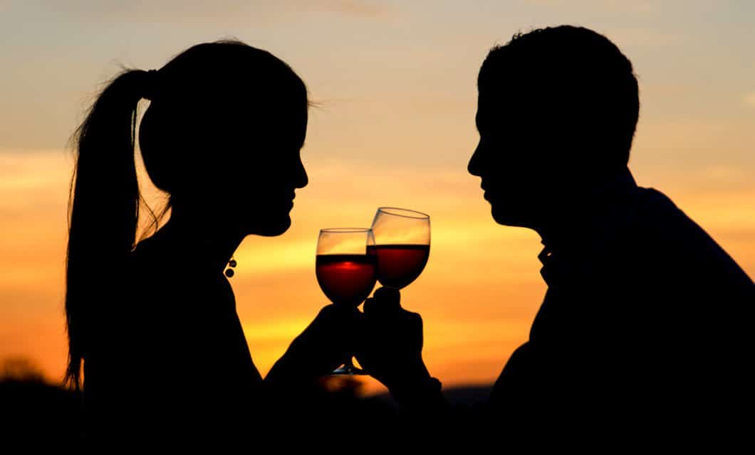 Silhouette of a couple clinking wine glasses together at sunset in Mendoza, with a warm orange and yellow sky—perfect for a romantic honeymoon in Mendoza.
