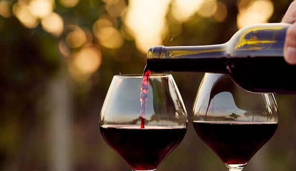 A close-up of red wine being poured into one of two glasses, with a blurred outdoor background and warm sunlight—perfect for toasting a South American honeymoon amid the region’s natural wonders.