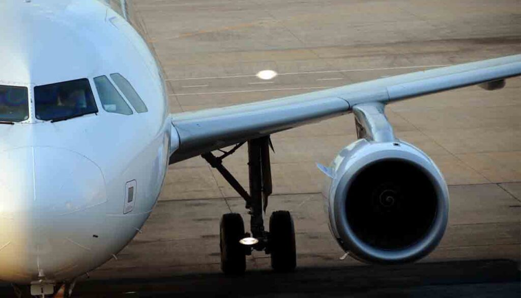 Close-up view of the front left side of a white airplane on the ground, showing the cockpit, left wing, engine, and landing gear on an airport tarmac—perfect for travel tips or jet lag advice before your next flight.