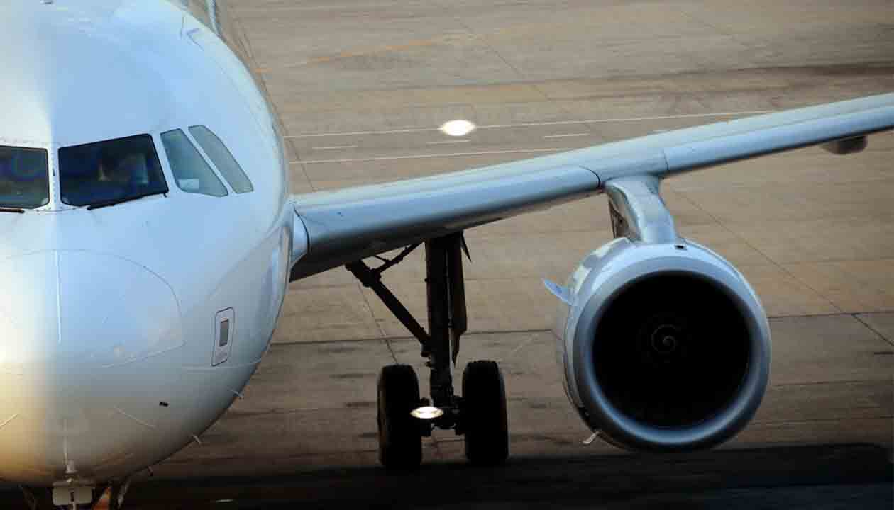 Close-up view of the front left side of a white airplane on the ground, showing the cockpit, left wing, engine, and landing gear on an airport tarmac—perfect for travel tips or jet lag advice before your next flight.